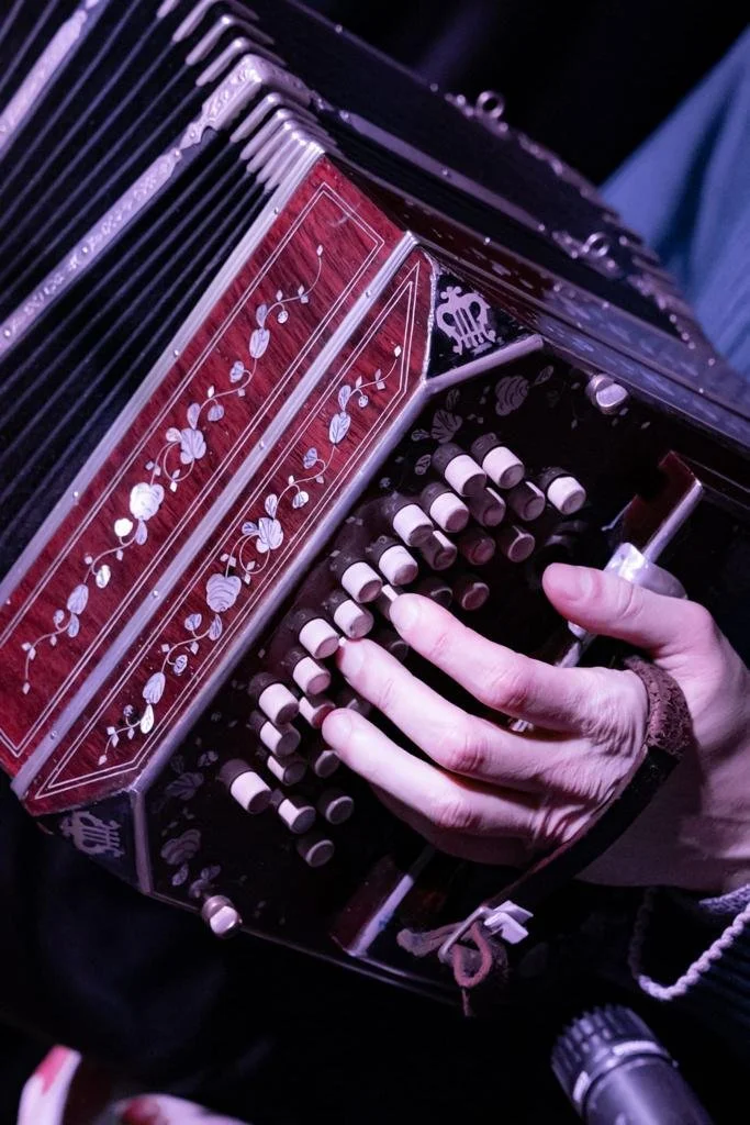 Black and white photo of Guillermo Willis playing Tango music with a bandoneon with a floral design on the front, holding the instrument with their left hand.