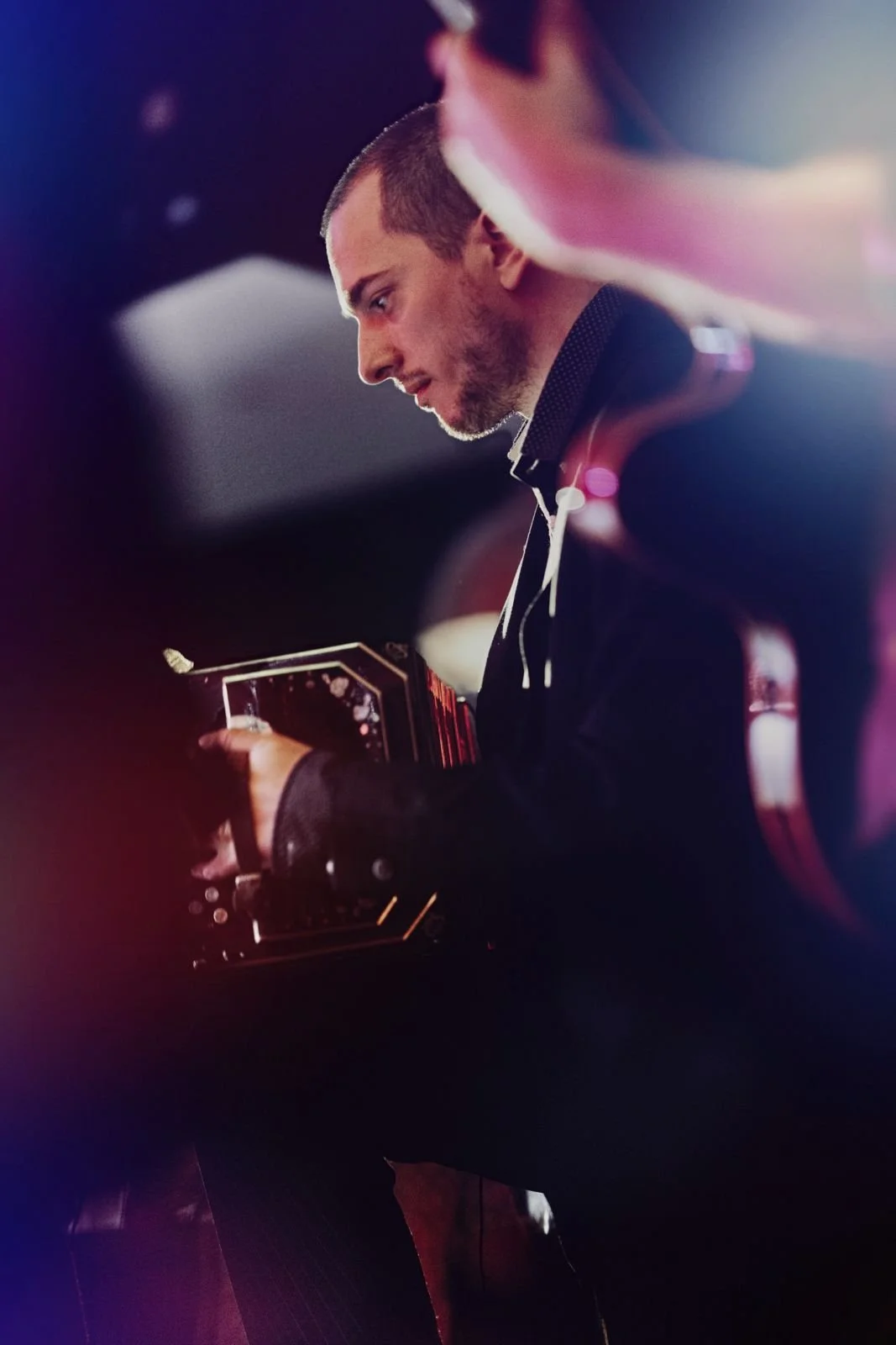 Guillermo Willis playing Tango in a bandoneon, looking down at his equipment in a dark, colorful setting.
