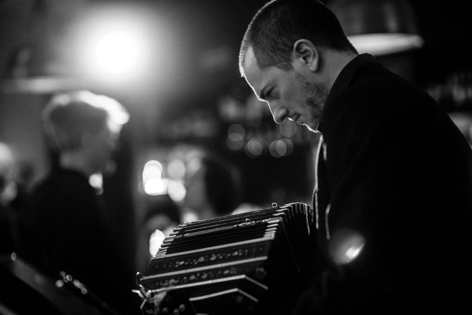 Guillermo Willis playing Tango in a bandoneon in a dimly lit setting with blurred background.