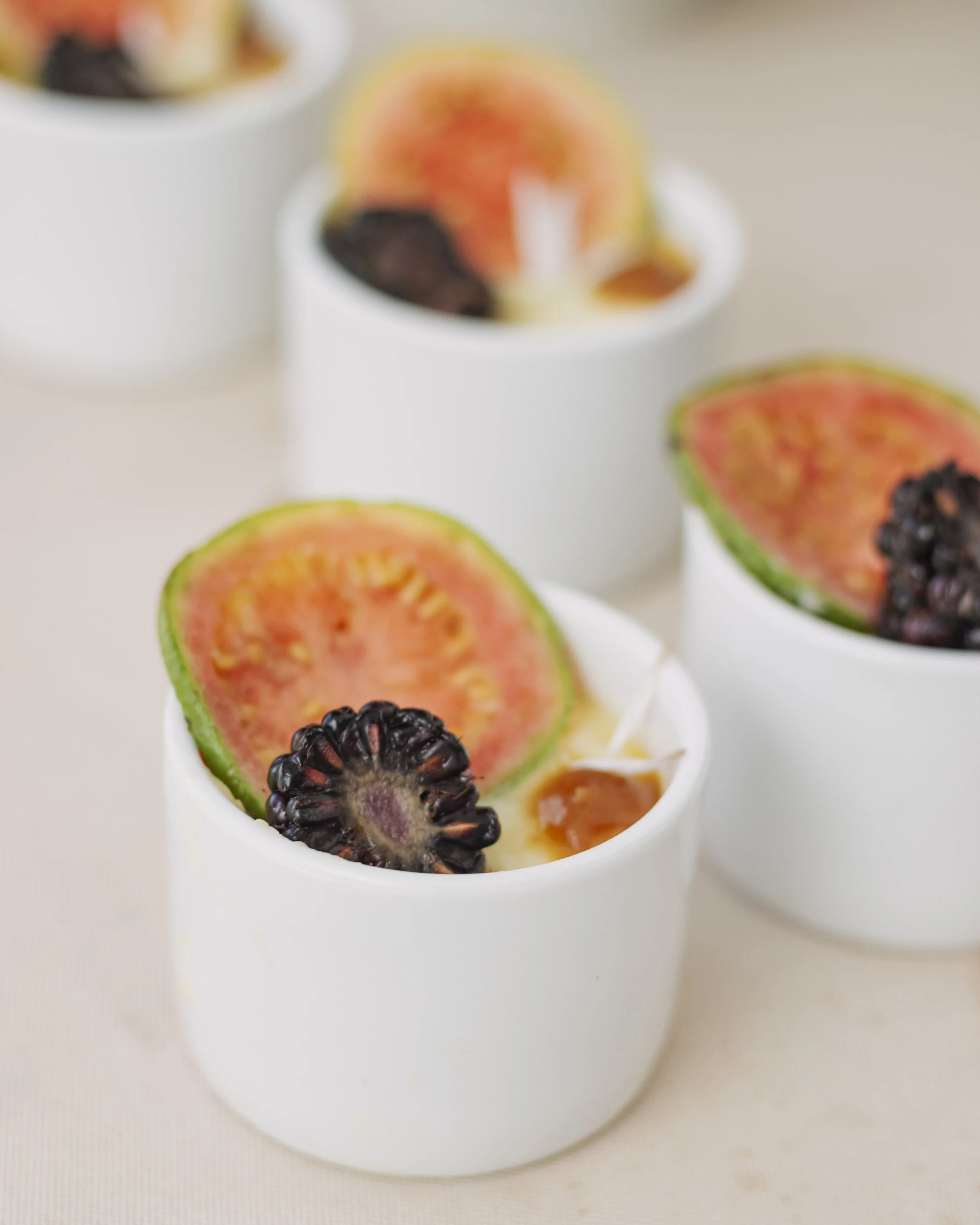 White cups with yogurt topped with slices of guava, blackberry, and honey.