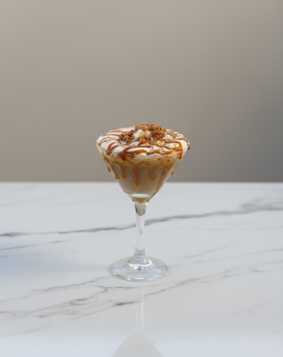 Caramel ice cream sundae with whipped cream and caramel drizzle in a glass on a white marble surface.