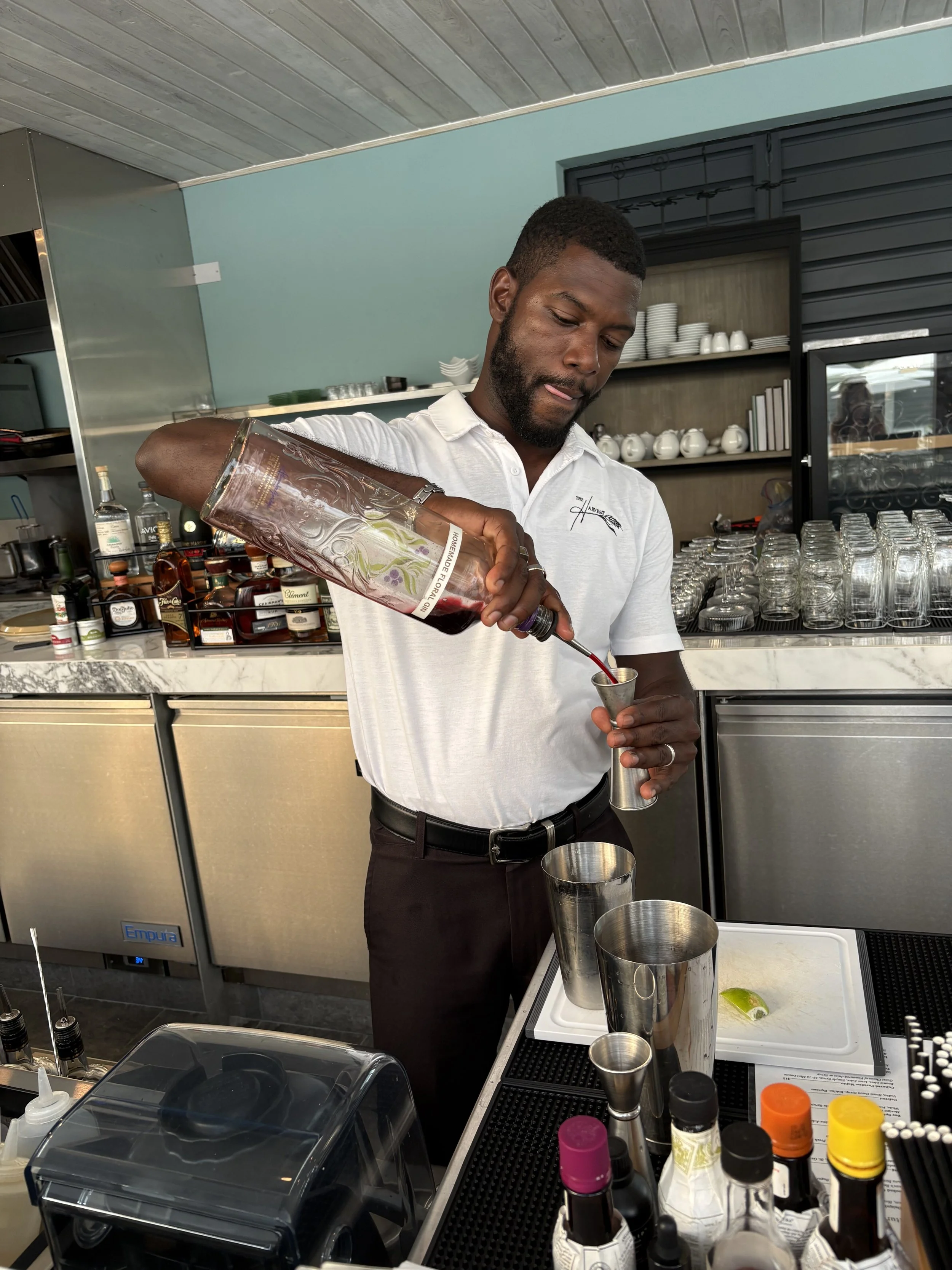 A bartender prepares a cocktail using a shaker and a liquid from a bottle in a bar setting.