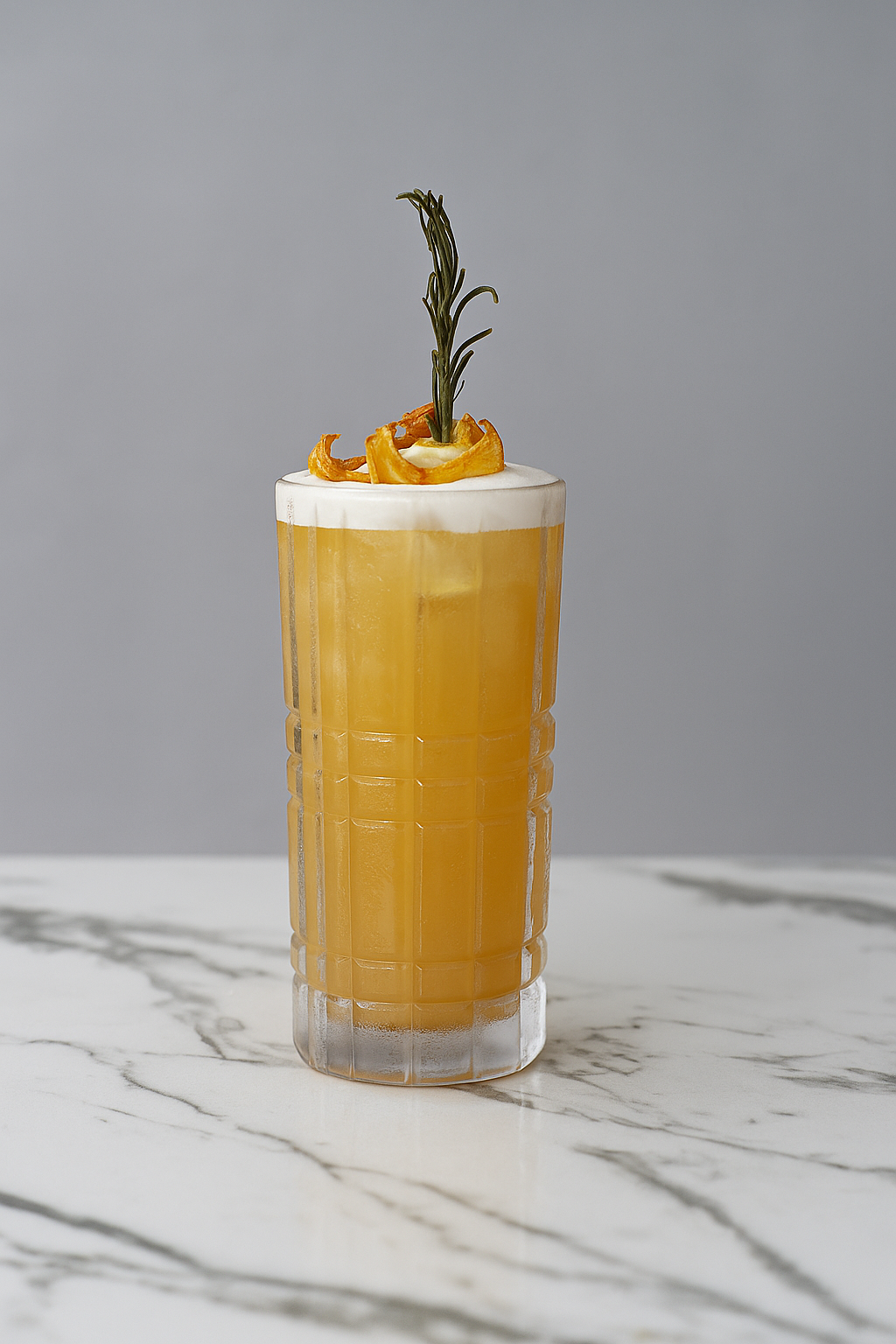 A tall clear glass filled with a yellow-orange beverage, topped with white foam, garnished with a sprig of rosemary and a candied lemon peel.