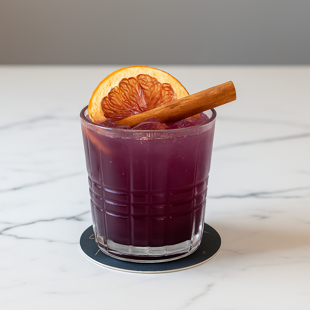 A glass of purple-colored beverage garnished with a dried orange slice and a cinnamon stick, sitting on a round coaster on a white marble surface.