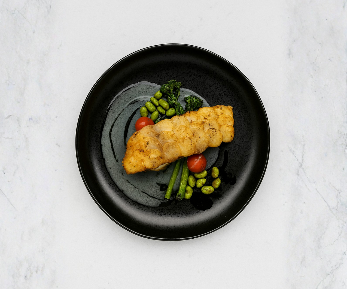 Fried fish fillet with green beans, cherry tomatoes, and snap peas on a black plate
