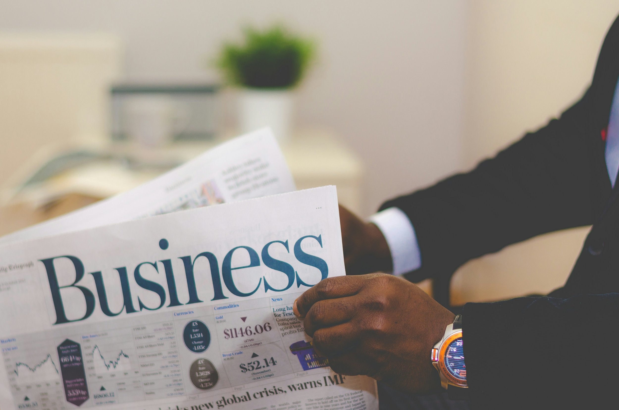 Person in a suit holding a business newspaper with financial data and charts.