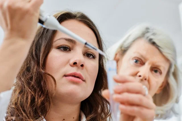 En ung kvinna som får en självständig injektion av en medicinsk professionell, med en äldre kvinna i bakgrunden i ett kliniskt miljö.
