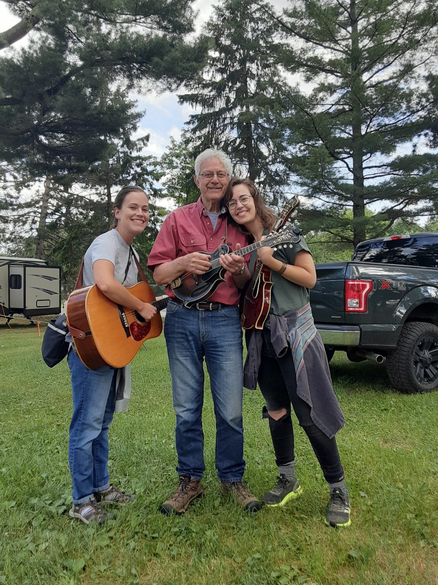 Liz (with guitar) and Emily (with mandolin) standing with Lloyd LaPlant at a bluegrass festival in Grand Rapids, MN