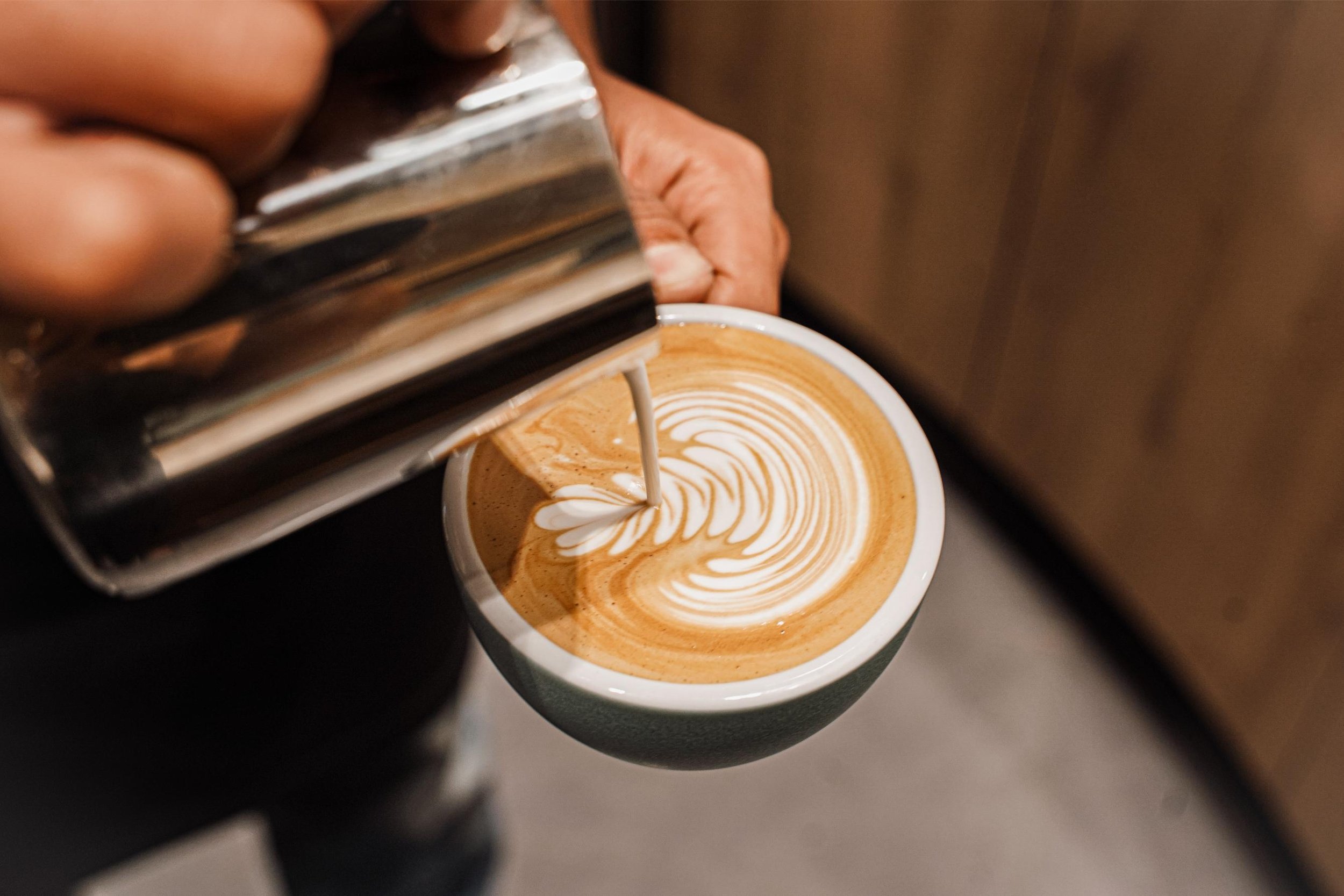 Coffee Bar at Centro Singapore, Shaw theatres, Lido cinema, Orchard Road. Close-up of a barista pouring steamed milk into a cup of espresso to create latte art, with a foam pattern forming on top of the coffee.