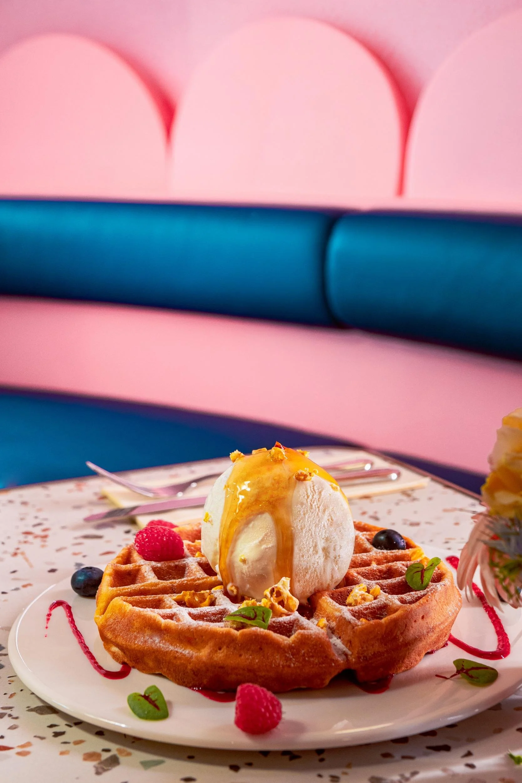 A plate with a waffle topped with a scoop of vanilla ice cream, caramel sauce, and garnished with raspberries, blueberries, and mint leaves. Grab yours at the Centro Gelato & Dessert Bar, located a Jem cinema, Shaw theatres in Jurong, Singapore