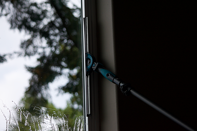 A person cleaning a window with a long-handled squeegee on a rainy day.