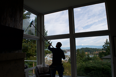 Person cleaning or inspecting a large window with a squeegee, overlooking a scenic outdoor view of trees and hills.