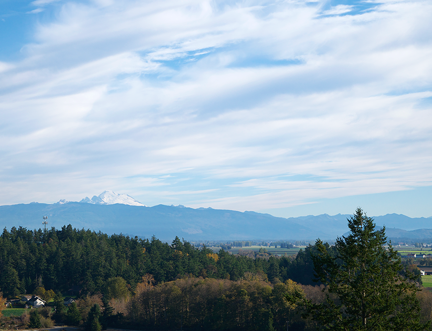 Scenic view of a mountain range with snow-capped peaks, green forested hills, and a partly cloudy sky.