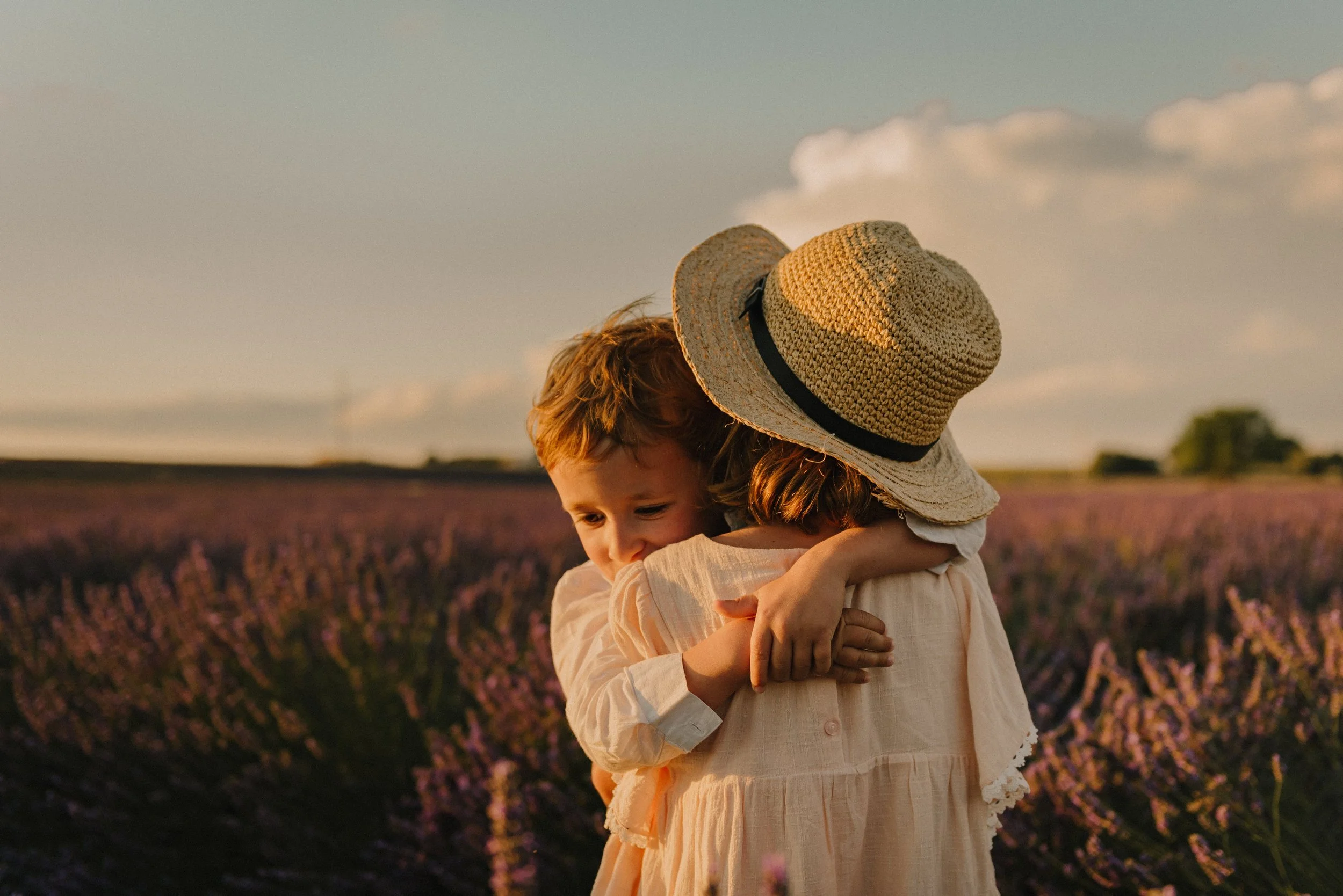 Two children hugging in a field of lavender with a sunset sky in the background.