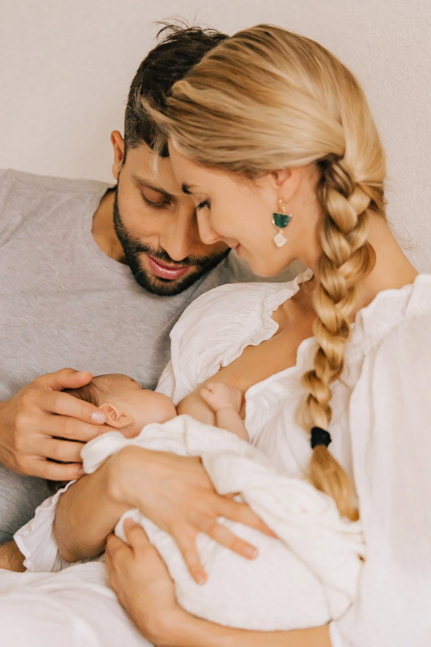 Family of three: mother, father, and newborn baby in a tender moment, with parents gently holding and looking at the baby.