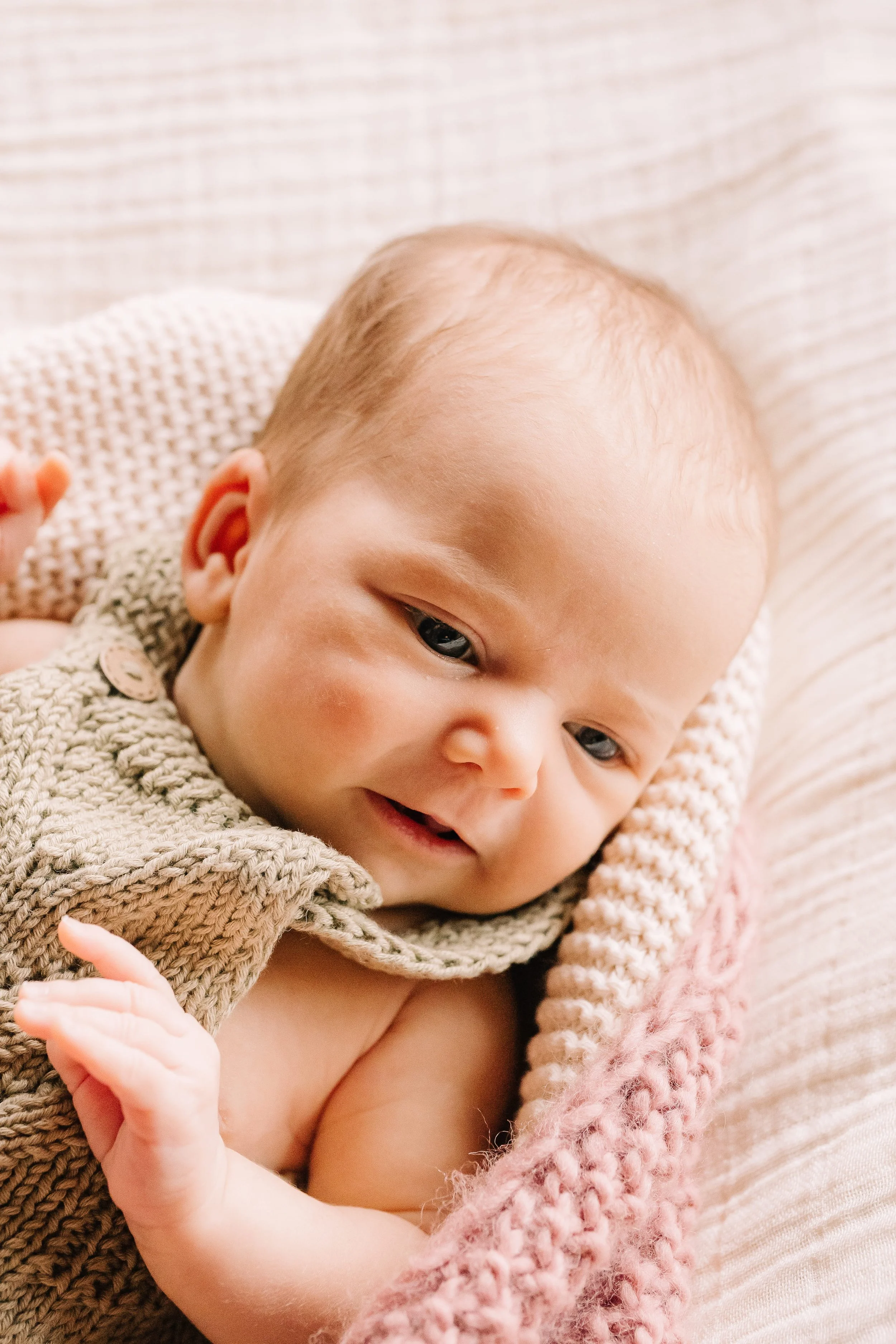 A close-up of a smiling baby lying on a textured blanket.