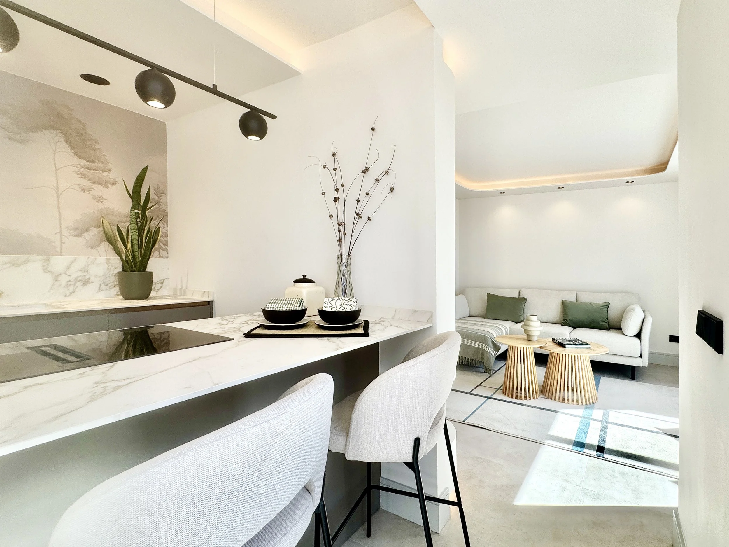 Vista del interior de una sala de estar con sillones blancos, mesas de madera, y decoración minimalista en colores neutros con algunos accesorios en verde.