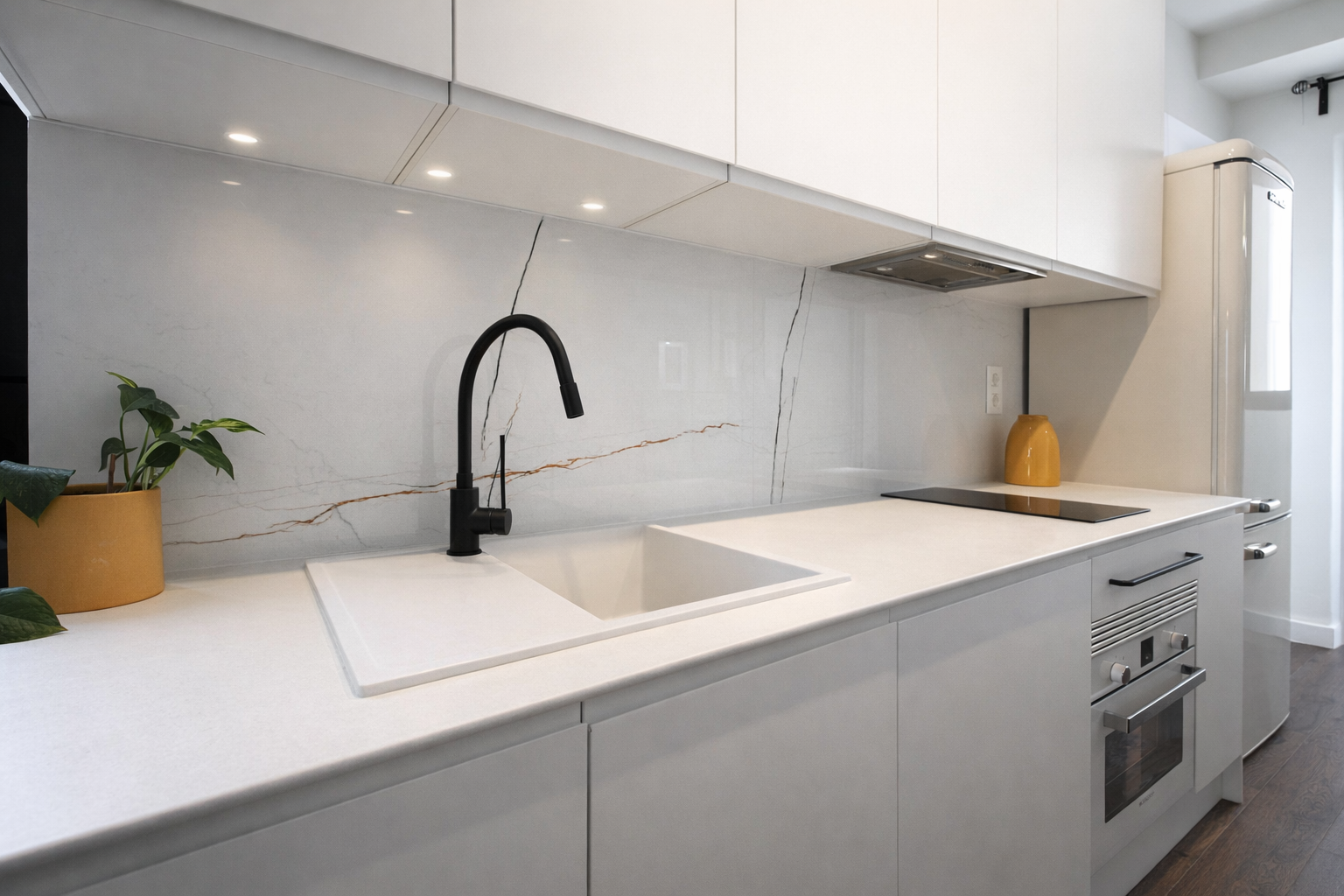 Cocina moderna con encimera blanca, fregadero y grifo negro, plantas en macetas amarillas, paredes de mármol y electrodomésticos blancos.