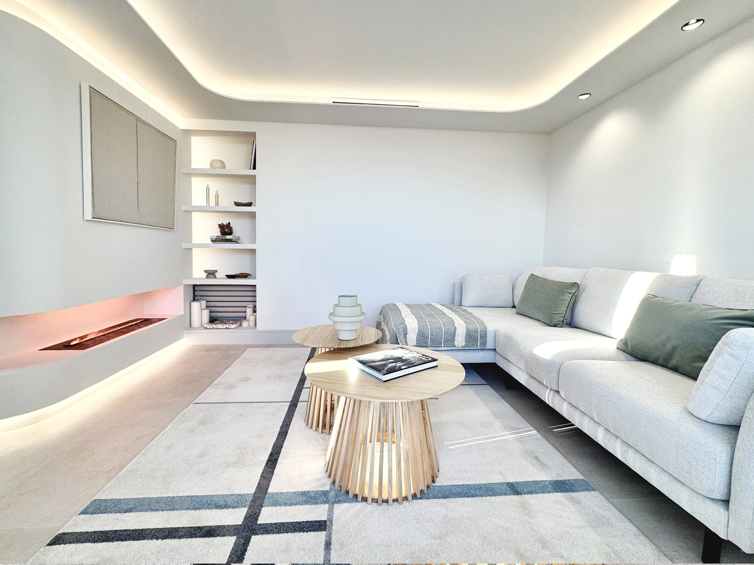 Sala moderna con sofá gris, mesas de madera, estantería blanca, paredes blancas, iluminación empotrada y decoración minimalista.