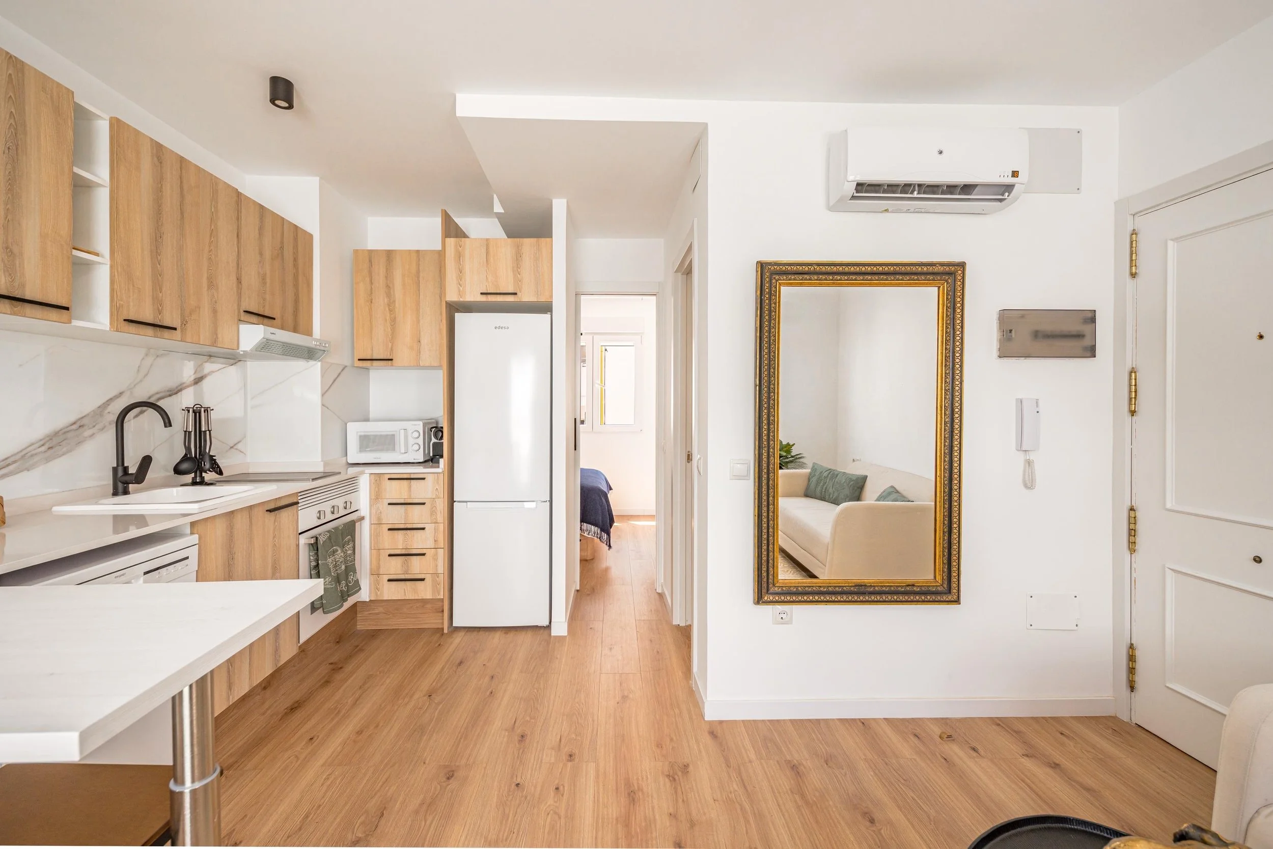 Vista del interior de un apartamento con cocina, comedor, sala de estar, espejo grande y aire acondicionado.