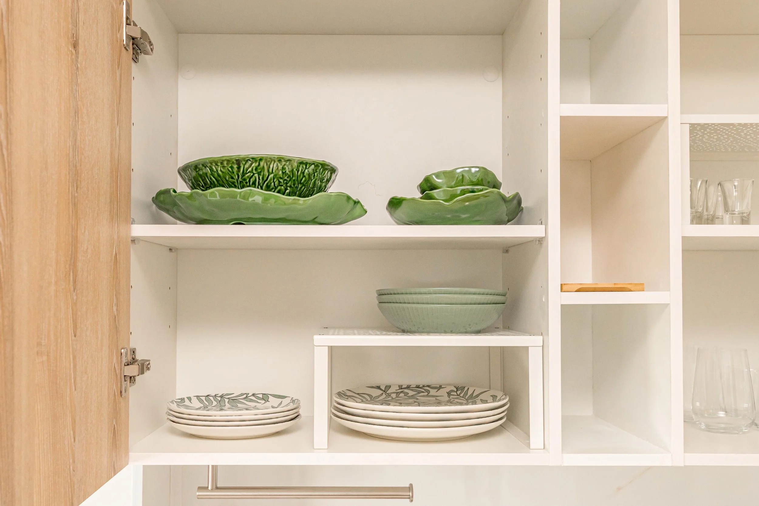 Estantes de vajilla con platos y fuente verdes y blancas en una alacena de cocina.