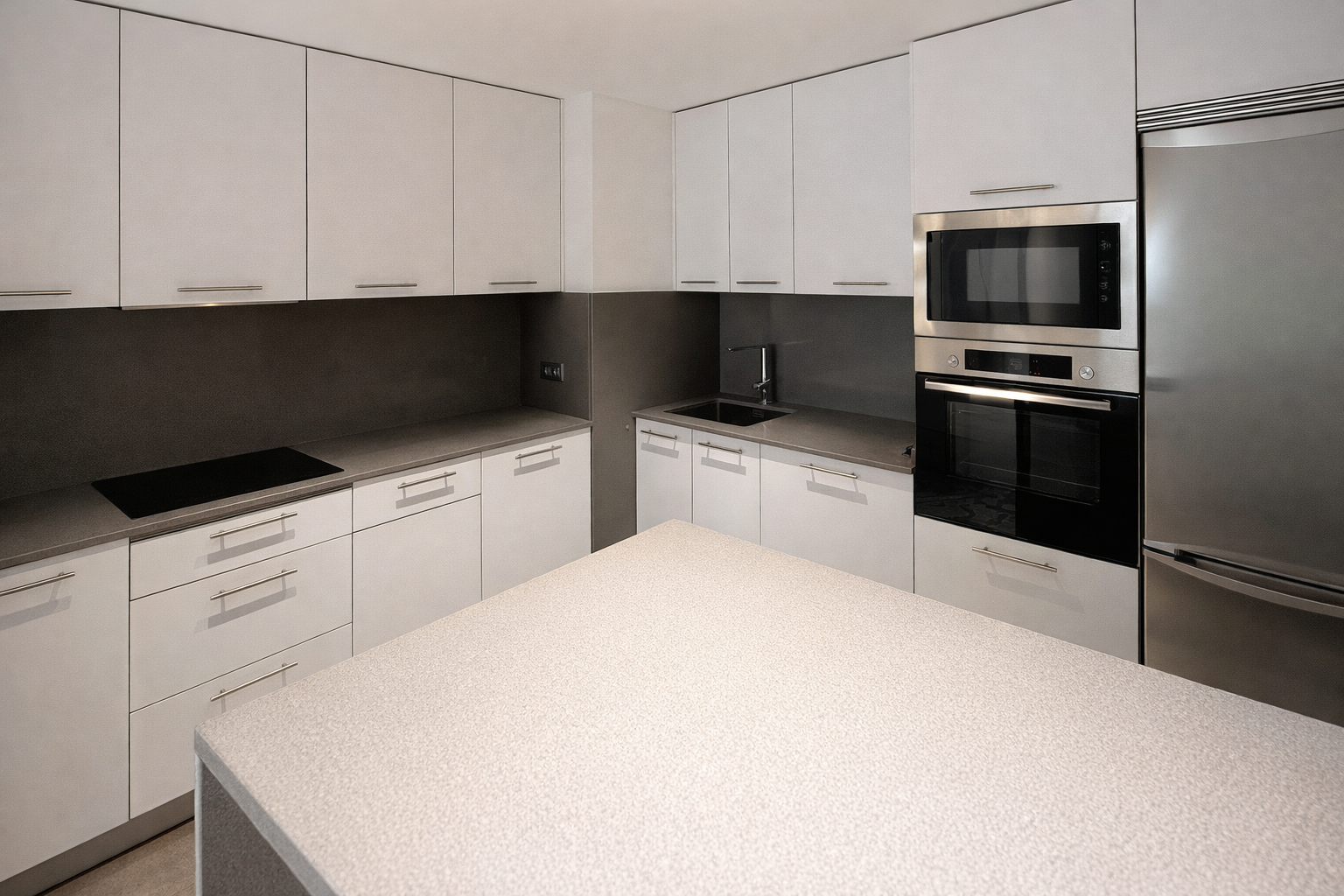 Cocina moderna con gabinetes blancos, encimera de superficie clara, estufa eléctrica, horno y microondas empotrados, fregadero junto a una pared gris y un refrigerador grande de acero inoxidable