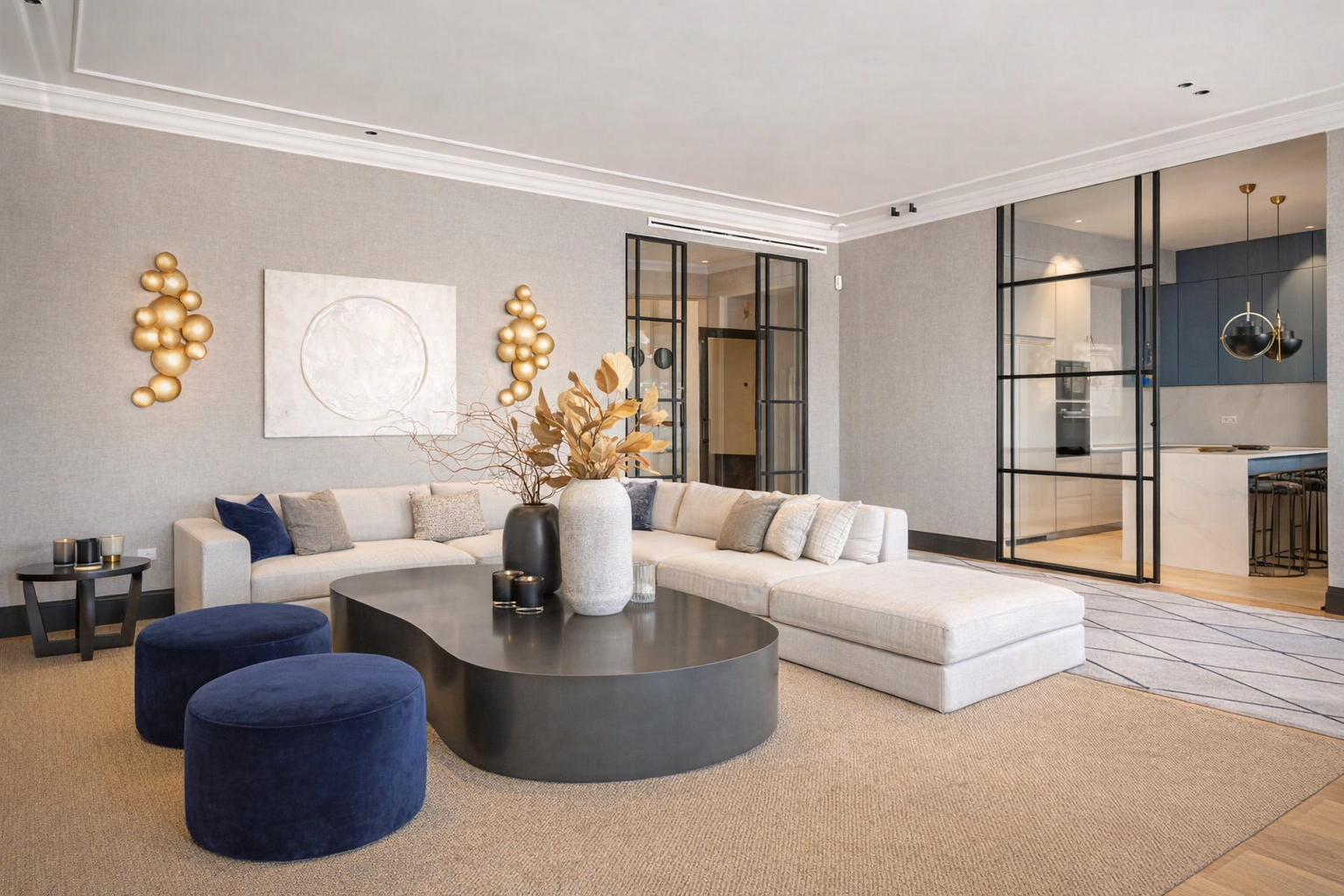 Sala de estar moderna con sofá beige, mesas negras, alfombra beige, decoración en tonos neutros y acento azul, con puertas de vidrio que comunican con la cocina.