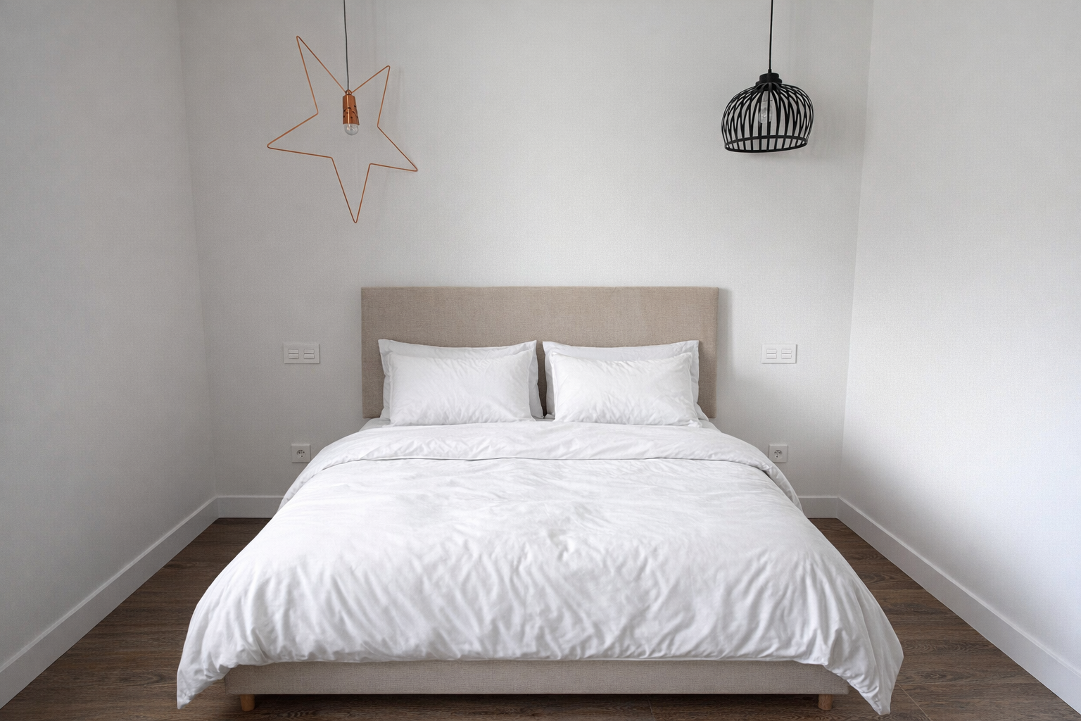 Habitación con cama doble con ropa blanca y cabecera beige, decorada con lámparas de diseño en las paredes, una en forma de estrella y otra en forma de jaula, paredes blancas y piso de madera
