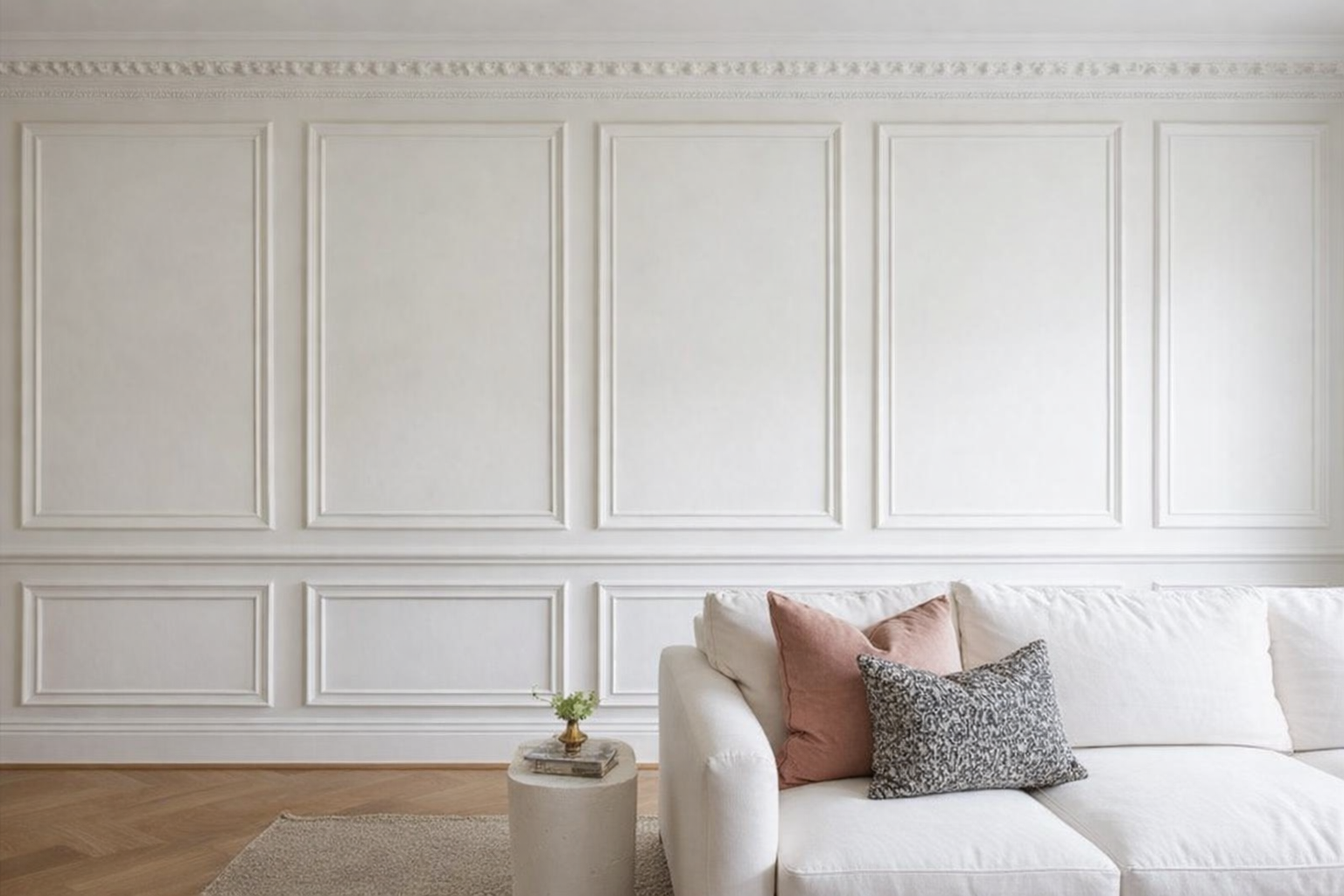 Sala moderna con muro decorativo en color blanco, sofá blanco con cojines en tonos rosa, negro y blanco, mesa auxiliar con planta y libros.