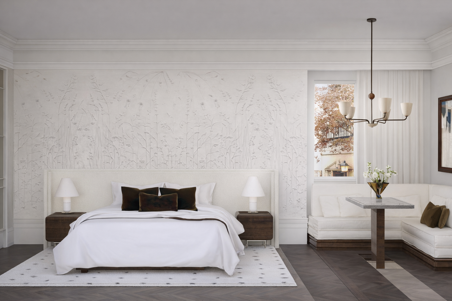 Habitación moderna con cama blanca, almohadas oscuras, lámparas de mesa a los lados y un sofá con mesa y jarrón con flores. ventanas que muestran árboles y viviendas exteriores.