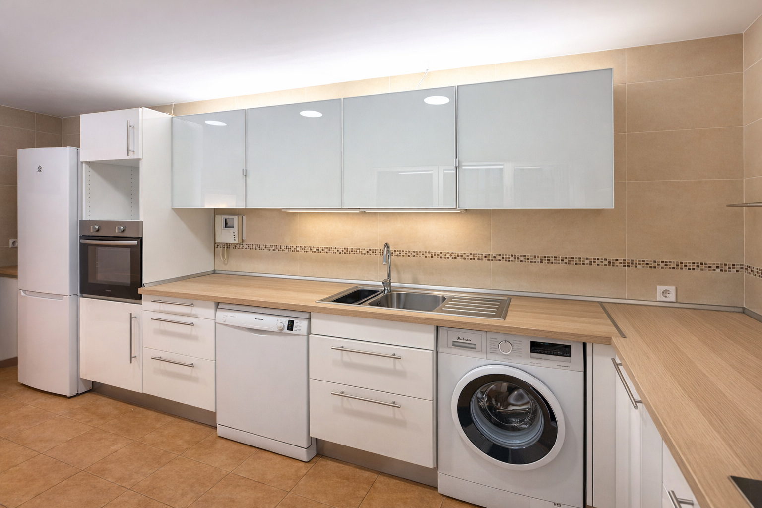 Cocina moderna con electrodomésticos blancos, gabinetes blancos, mesada de madera, y paredes de azulejo beige.