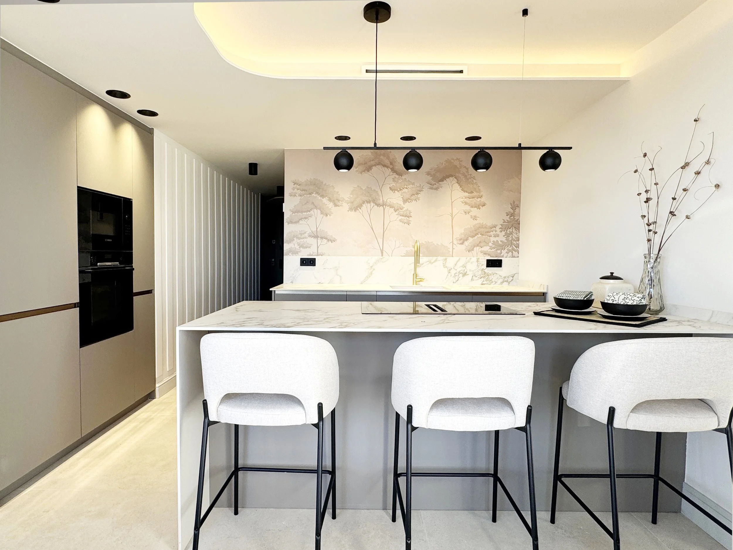 Cocina moderna con isla, paredes decoradas, utensilios y sillas blancas.