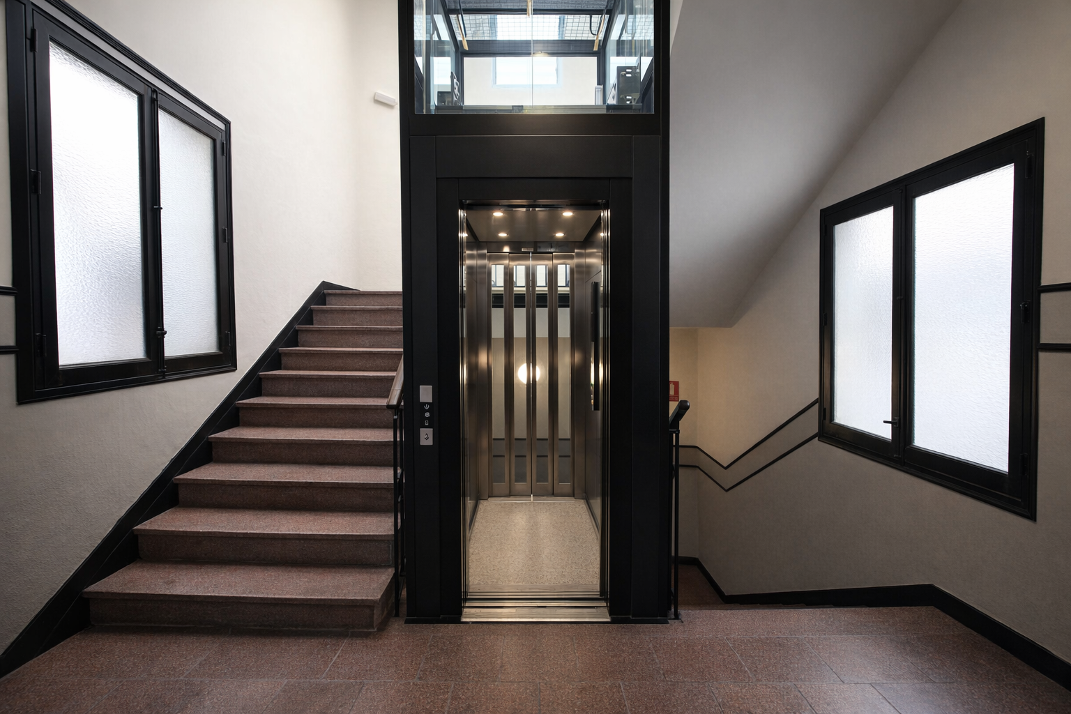 Ascensor y escaleras en un edificio con ventanas y paredes claras