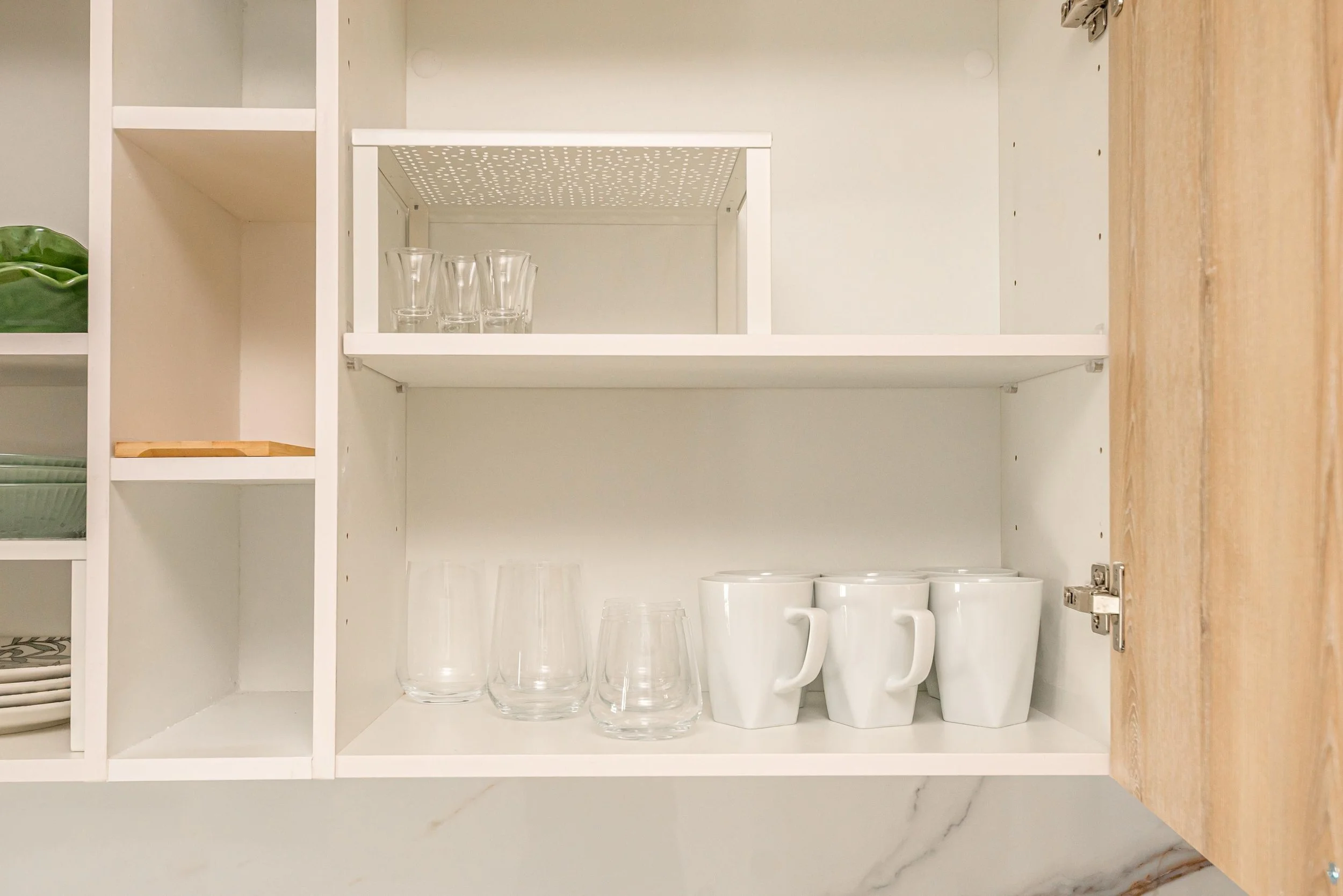 Gabinetes abiertos con vasos de vidrio y tazas blancas.