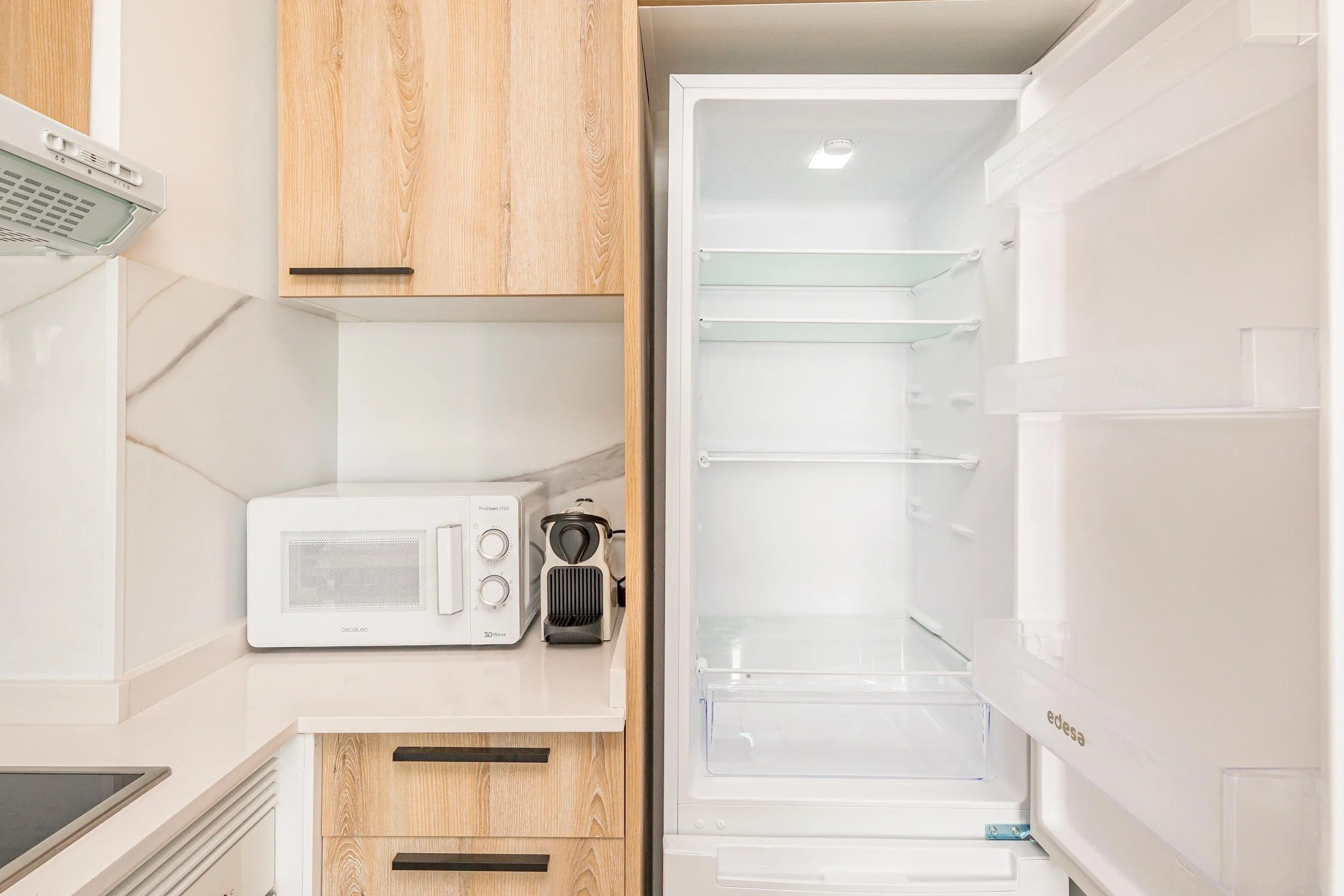 Nevera abierta en una cocina con puertas de madera y electrodomésticos blancos.