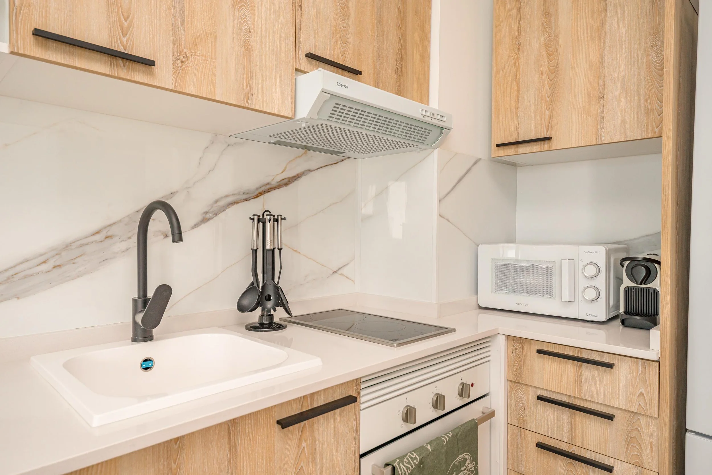 Cocina moderna con encimera, fregadero, microondas, cafetera, y armarios de madera.