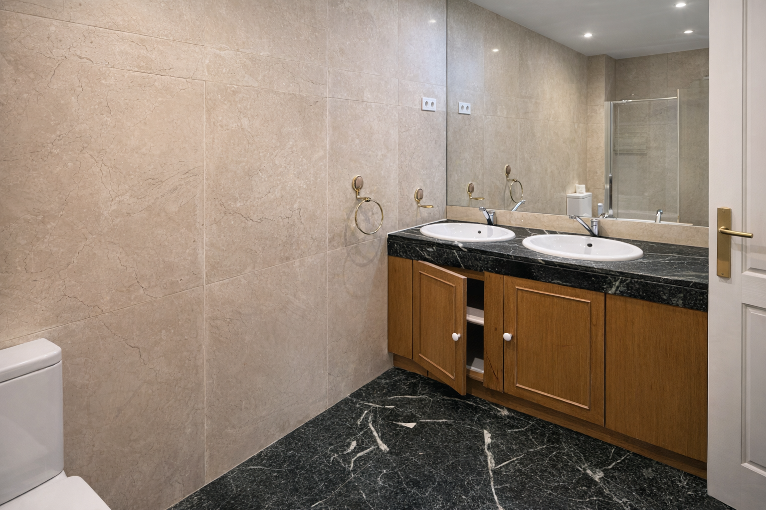 Baño con lavabo doble, espejo grande y paredes de azulejo beige.