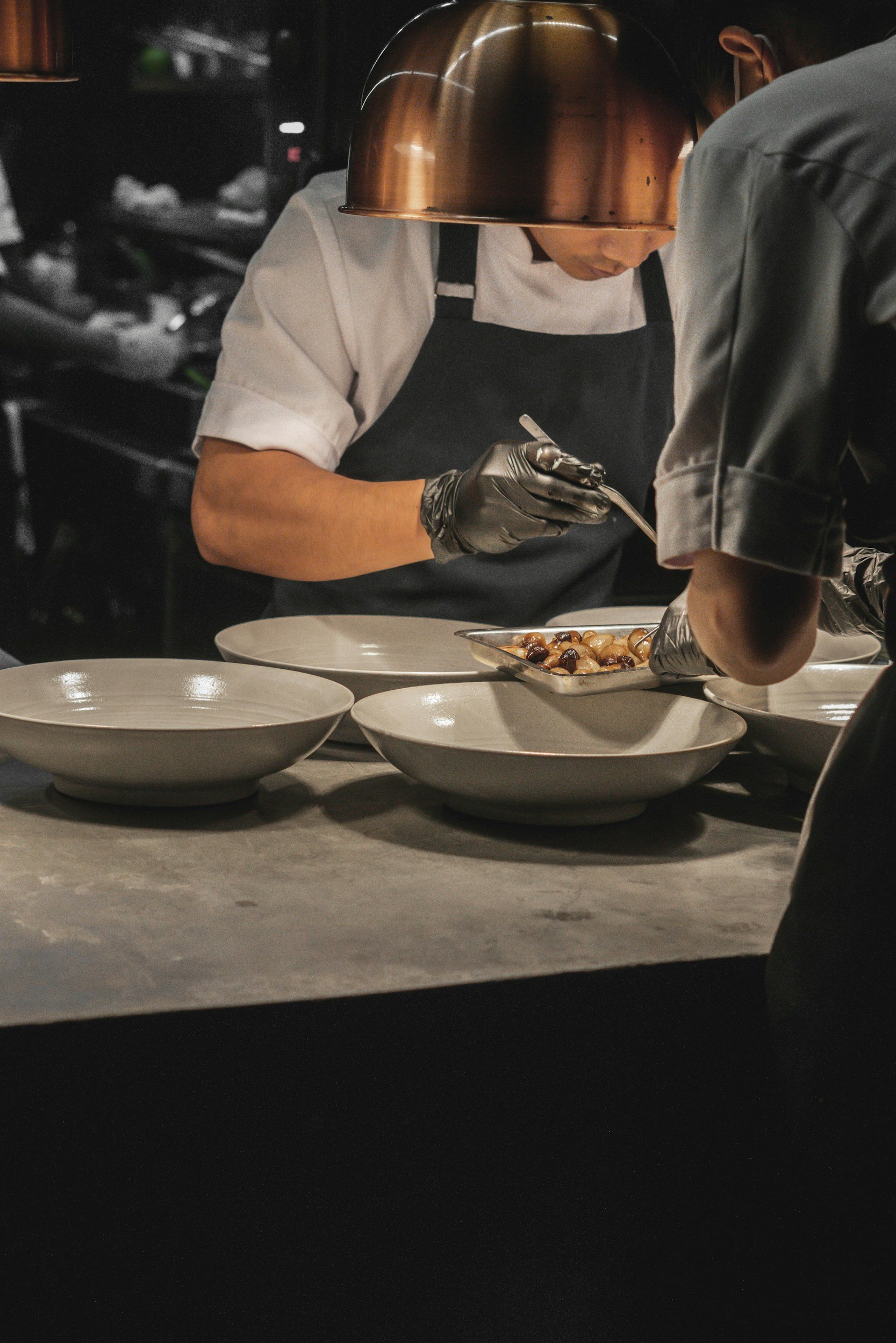 Chef preparing plated dishes in a professional kitchen, with empty bowls on the counter in the foreground.
