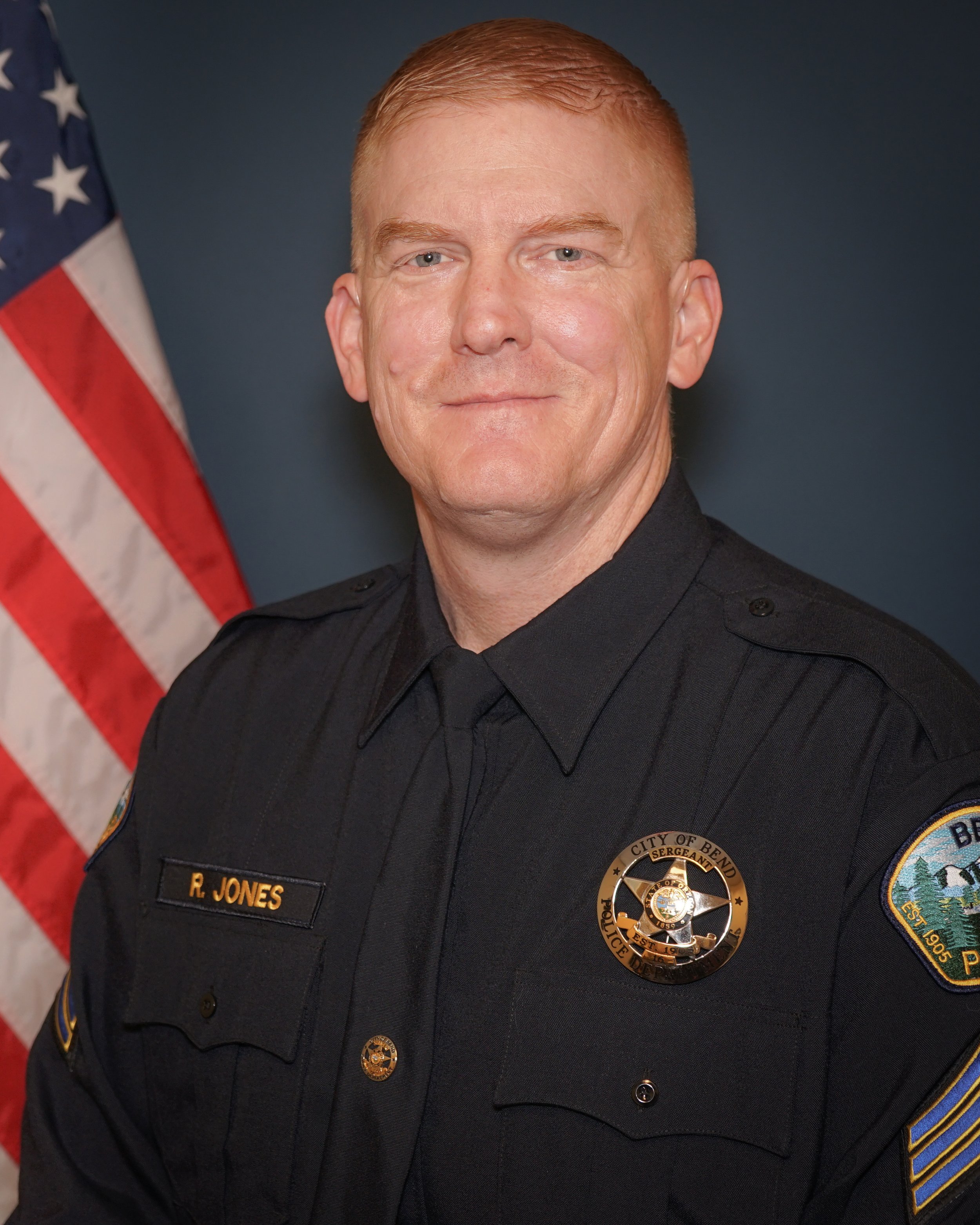 man with dark blue police uniform american flag in background Bob Jones