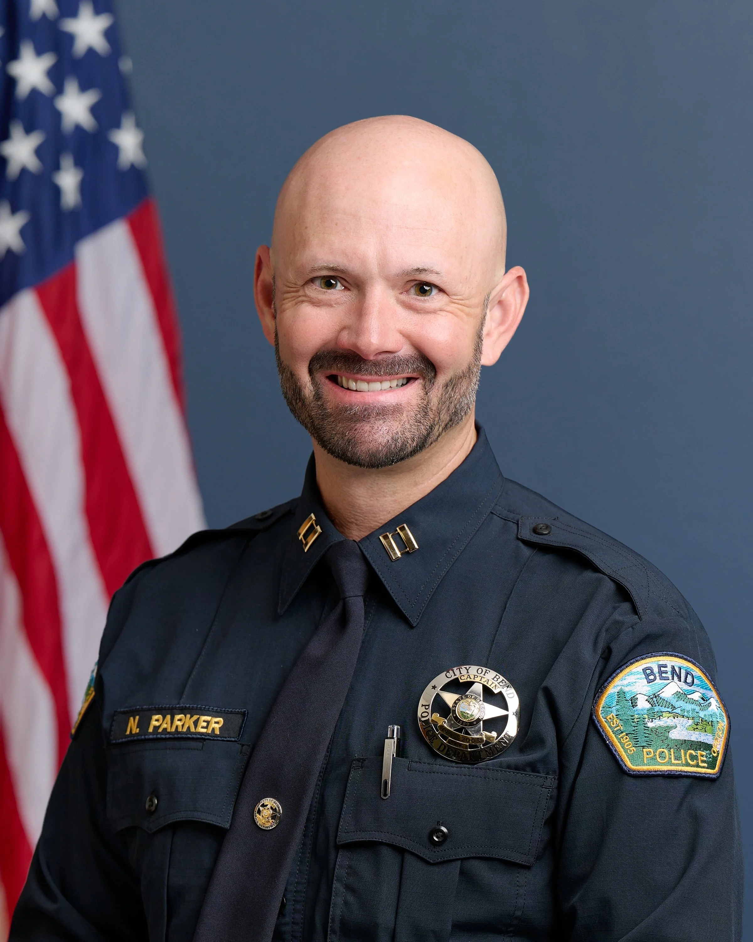 man with dark blue police uniform american flag in background Nick Parker