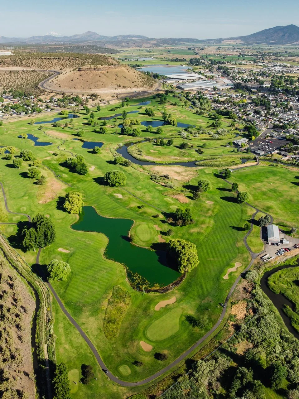 Aerial view of a lush green golf course surrounded by houses, water and canyon.