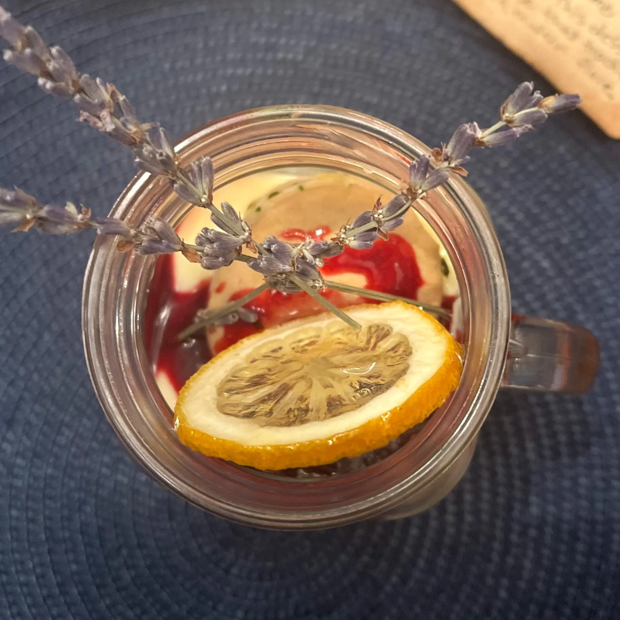 View from above of a mason jar filled with a beverage, garnished with a slice of lemon and sprigs of lavender, on a dark textured surface.