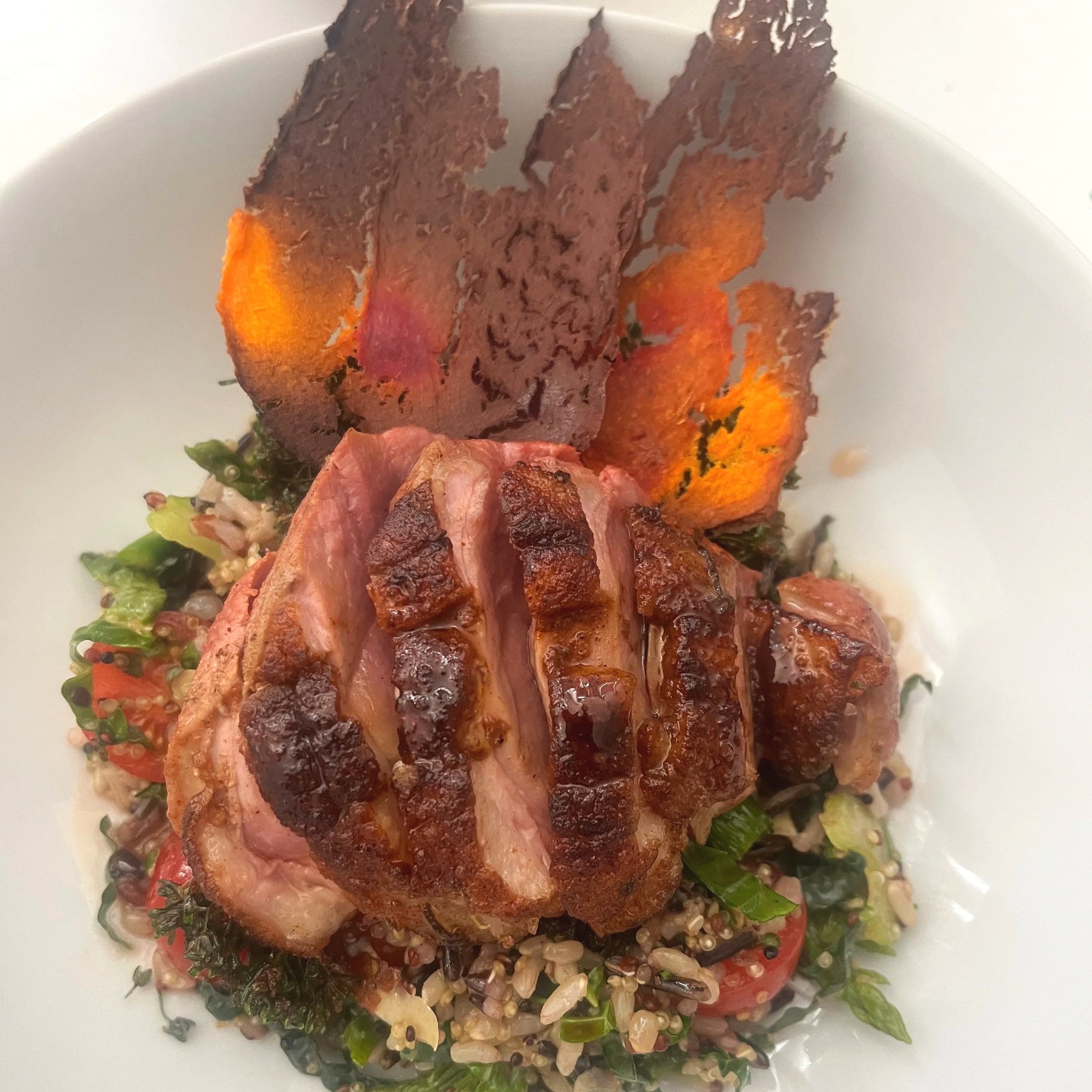 Grilled sliced chicken breast served on a bed of quinoa salad with cherry tomatoes, herbs, and roasted vegetable chips.