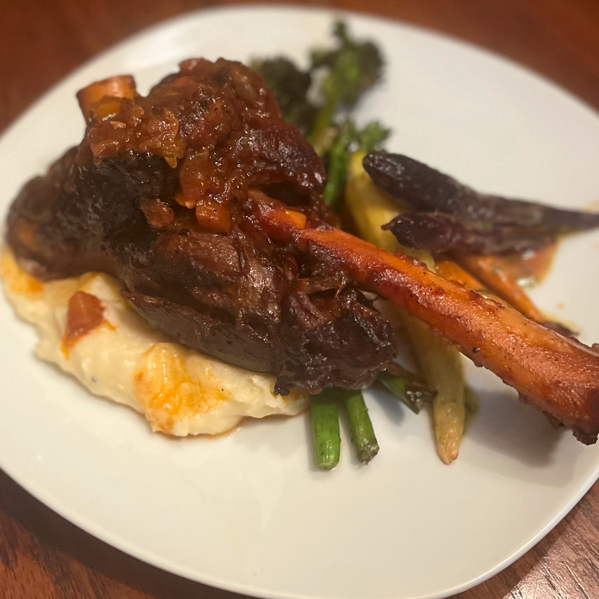 Plate of roasted vegetables including carrots, eggplant, and a dark leafy green, served over mashed potatoes with a meat patty topped with a thick brown gravy and vegetables