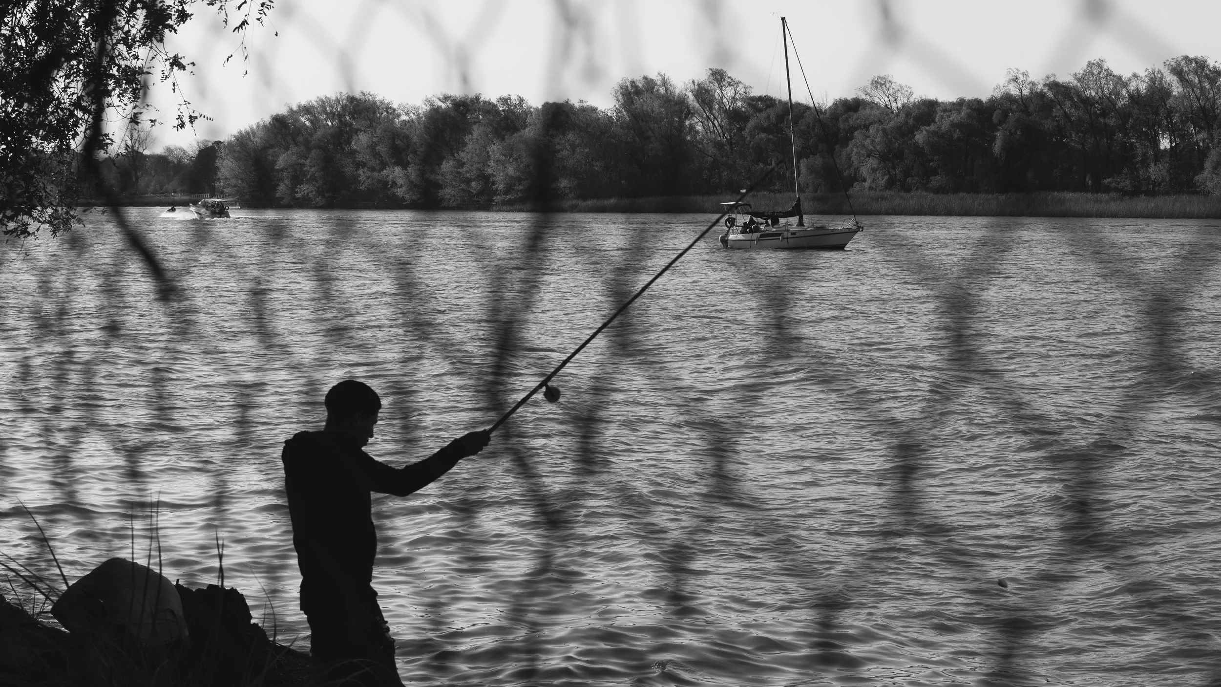 Fisherman behind a fence in a river with cruising sailboats