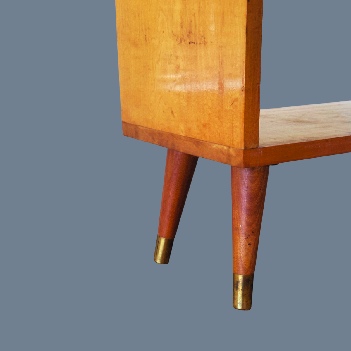 Close-up of mid-century modern wooden furniture leg with brass tip, featuring a natural wood finish and slightly tapered shape.