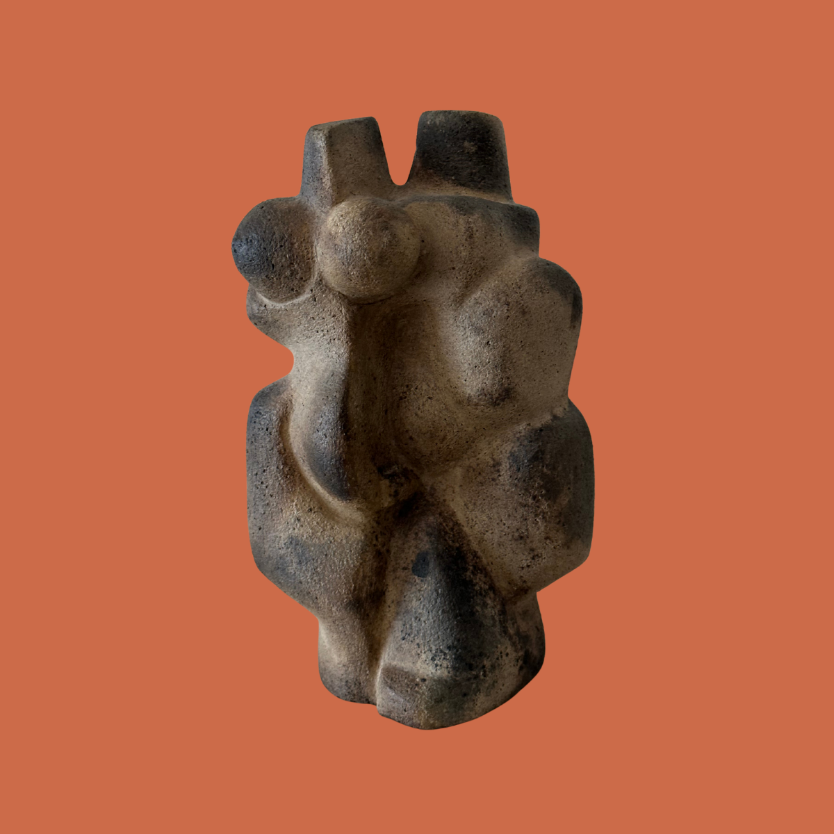 A stone sculpture of a stylized human figure with exaggerated features, abstract and modern art style, against an orange background.