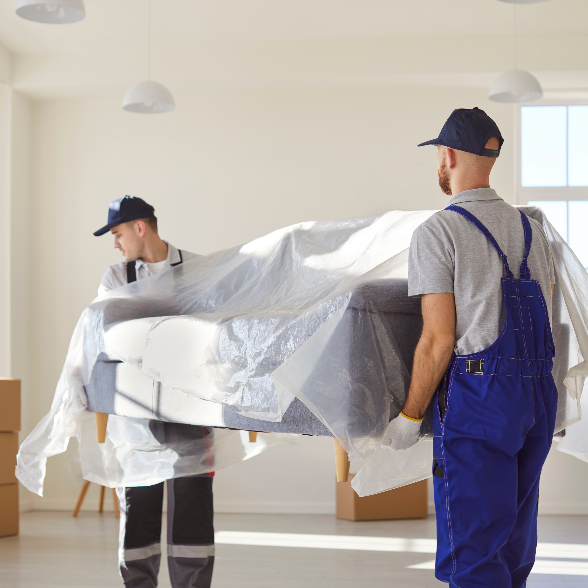 Two workers carefully carrying a large wrapped piece of furniture, representing safe removal of oversized household items.