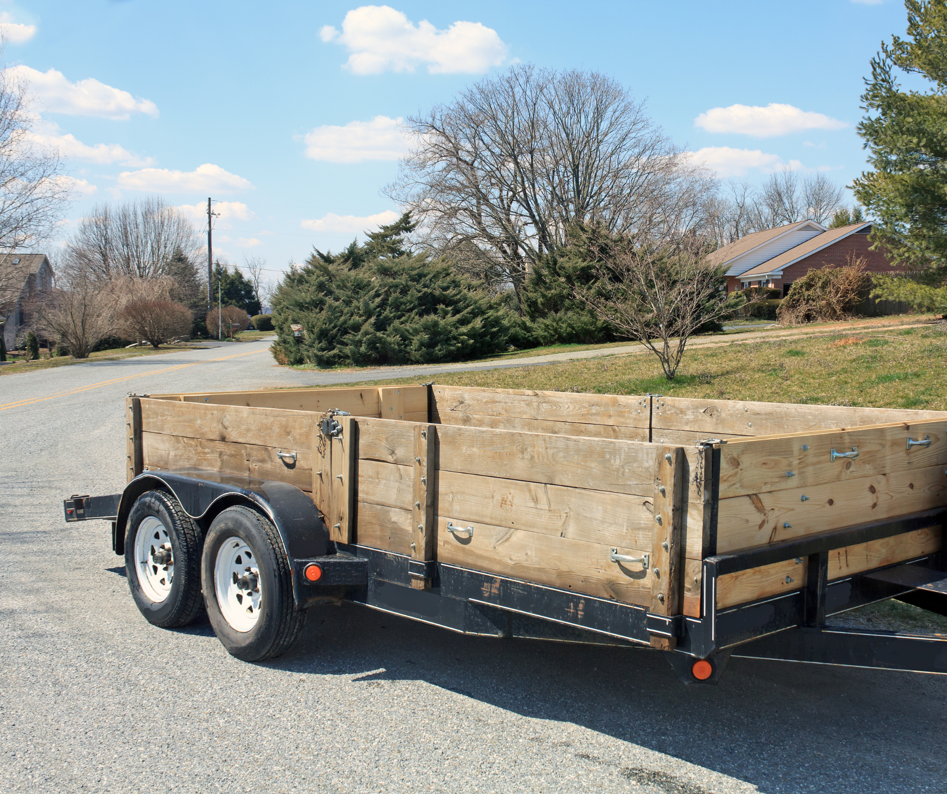 A flatbed utility trailer ready to move estate items in a suburban neighborhood, with trees and houses in the background.