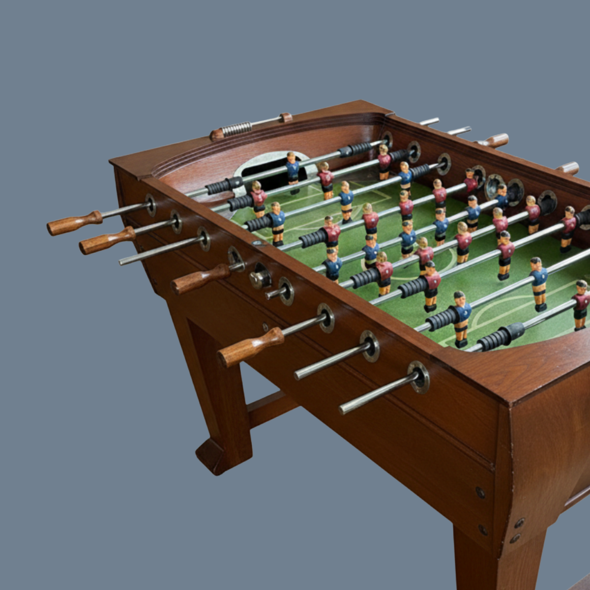 A vintage wooden foosball table for sale as part of an estate sale, with metal rods and colorful player figures on a green field.